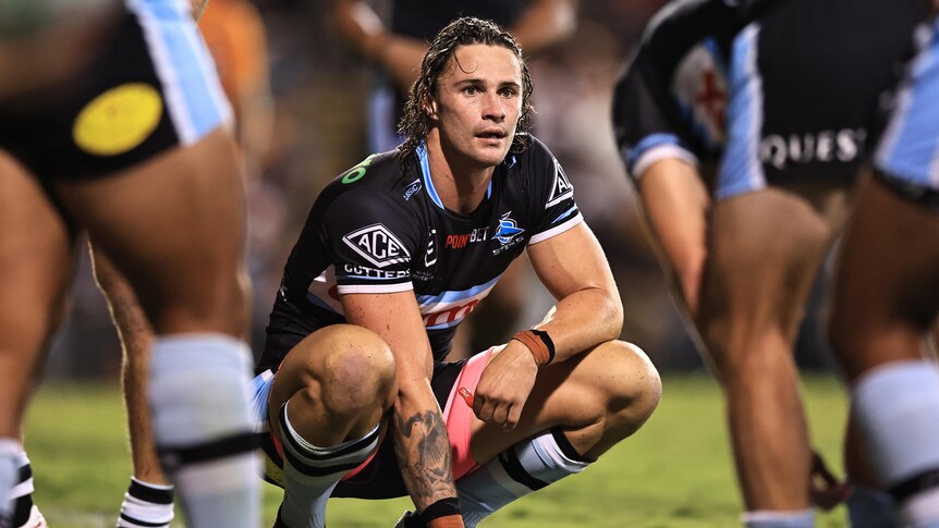 NRL player Nicho Hynes on his haunches, looking exhausted and sweating during a night match against the Tigers
