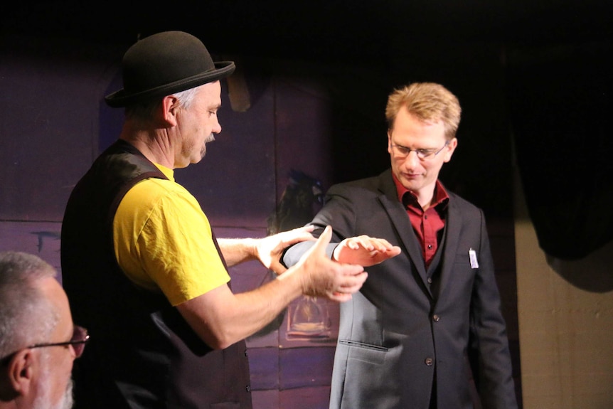 A bowler-hatted magician performs a trick with a volunteer.