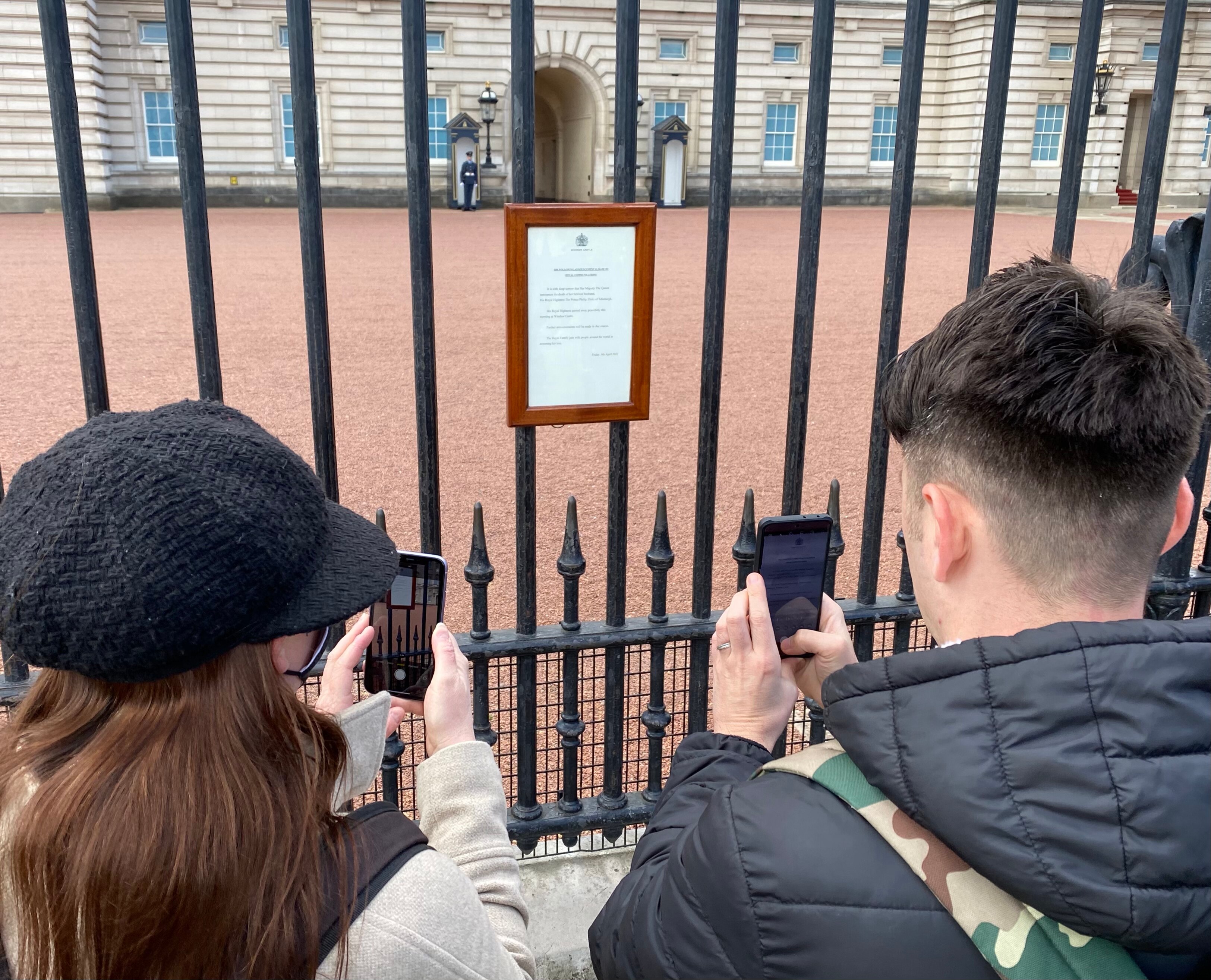Two people photograph the notice indicating Prince Philip's death outside Buckingham Palace