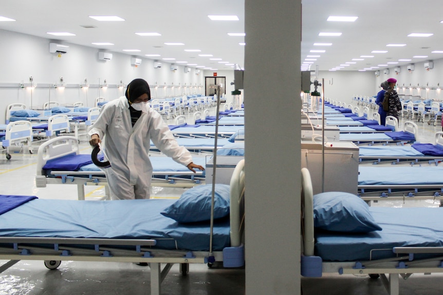 A worker prepares one of dozens of empty beds in a hospital ward.