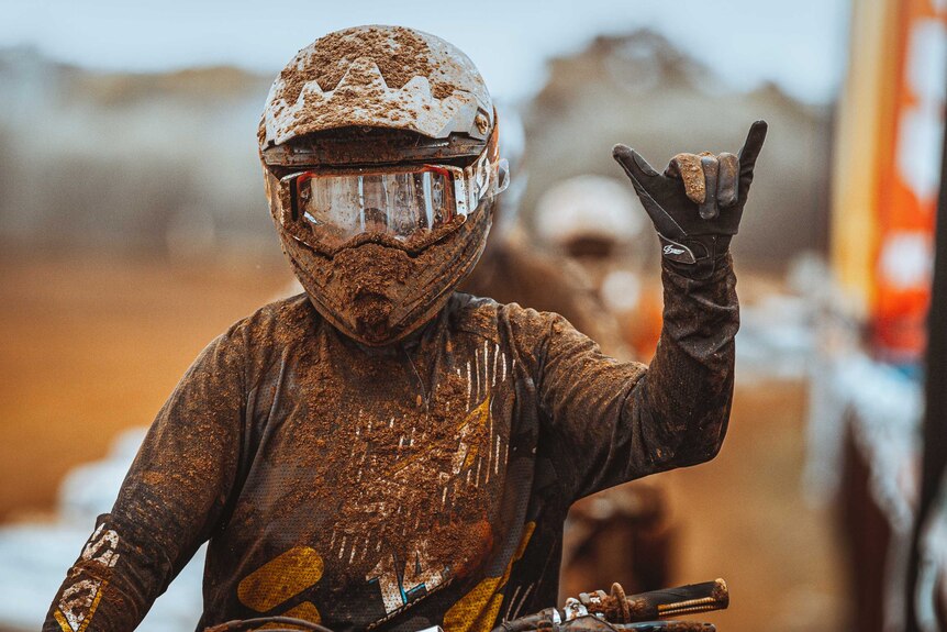 A teenager covered in mud with a motorbike helmet showing the 'rock on' symbol.
