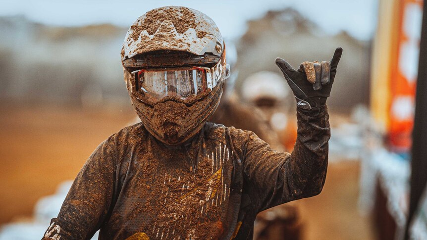 A teenager covered in mud with a motorbike helmet showing the 'rock on' symbol