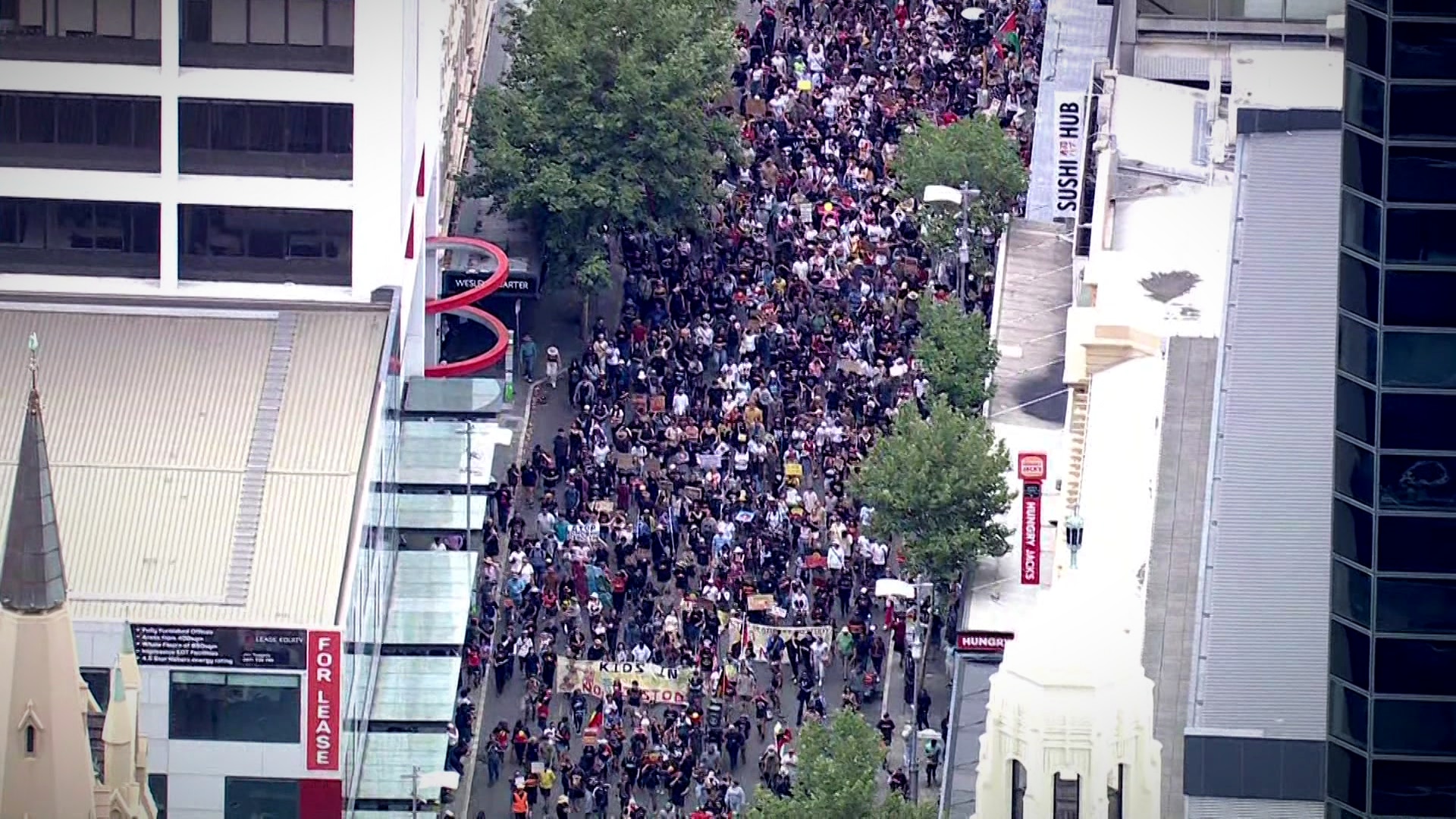     Um grande grupo de pessoas marcha por uma rua.