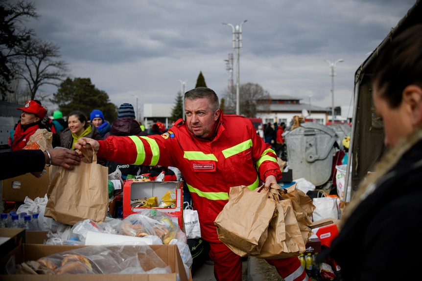 A man in orange outfit hands out paper bags. 