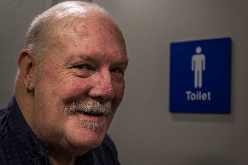 Trough Man standing outside a male toilet.