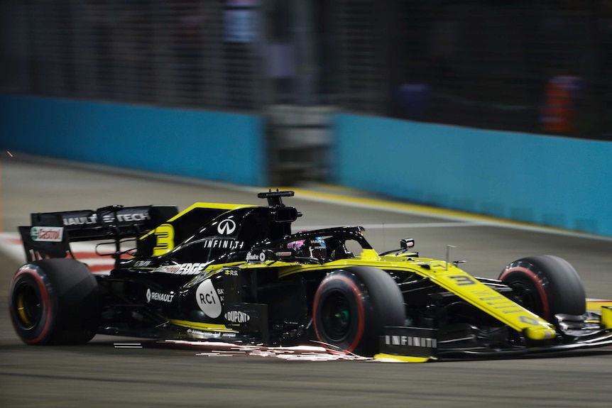 Daniel Ricciardo drives in a black and yellow formula one car with sparks coming from the front wing
