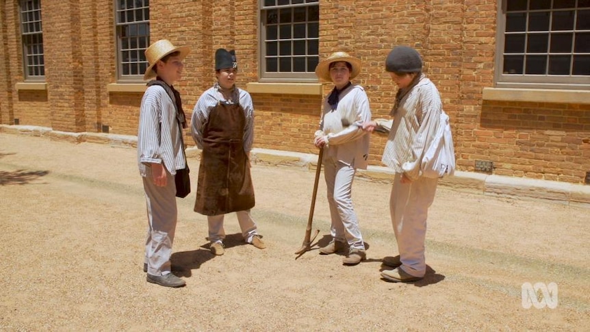 Four boys in period clothing stand outside building