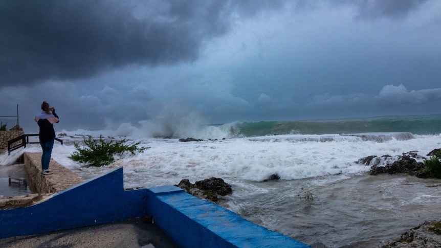 A woman watches on as waves break. 