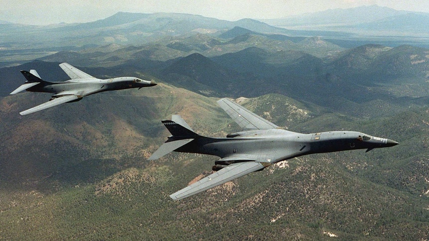 A pair of B-1B Lancer bombers soar over Wyoming with hills, clouds in background.