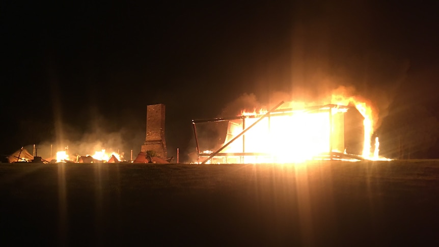 Blazing fire at night time with remains of a large chimney and walls around it in collapsed state. 