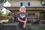A woman with tattoos standing outside a wrecked house.