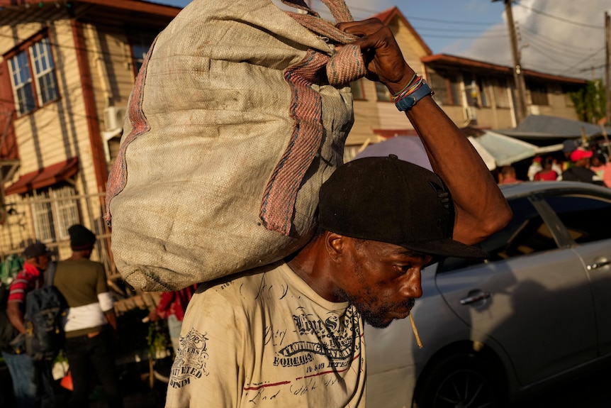 A man carrying a full sack of fruit on his back. 