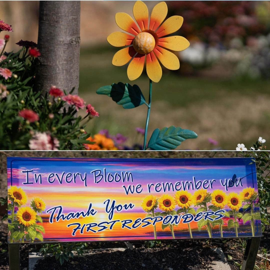 A sign in a flower-filled garden bed reads 'In every bloom we remember you. Thank you first responders'. 