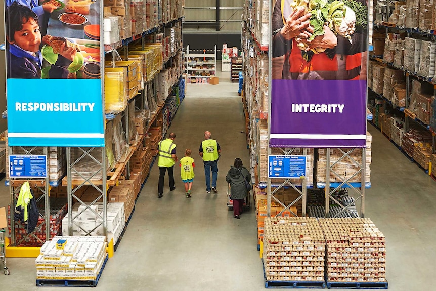 Staff in fluro vests and customers walk through a Foodbank warehouse