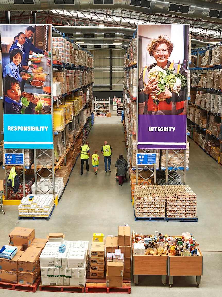 Staff in fluro vests and customers walk through a Foodbank warehouse