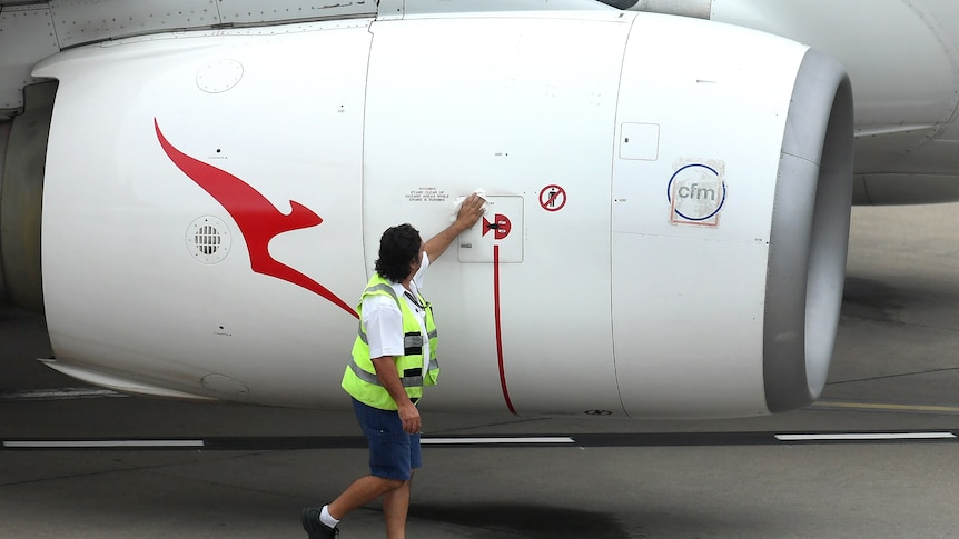 A Qantas worker wearing a high-vis vest wipes down an engine that has a red kangaroo logo on it.