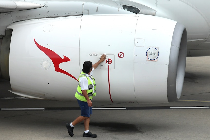A Qantas worker wearing a high-vis vest wipes down an engine that has a red kangaroo logo on it.