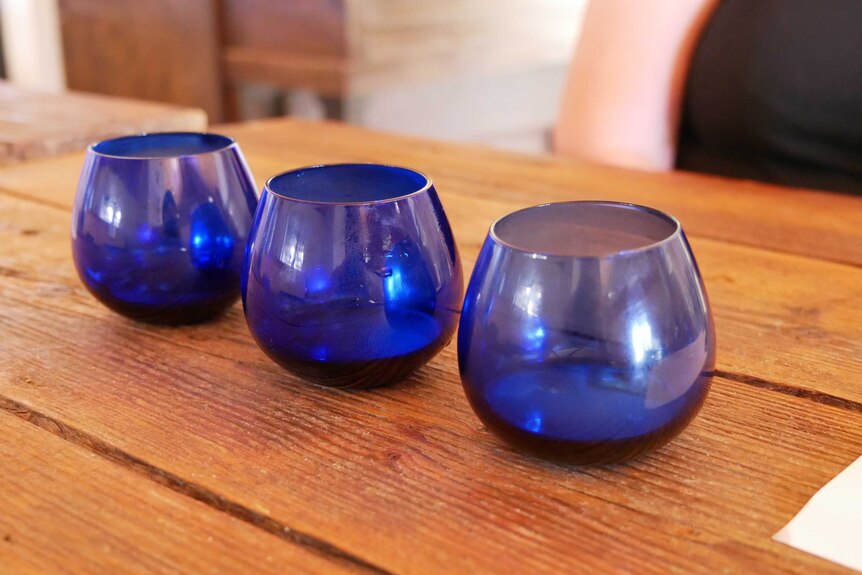 Three blue tumblers sitting on a wooden bench.