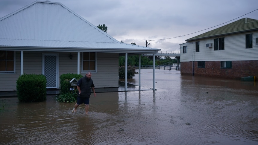 A man wades through flood waters outside a house