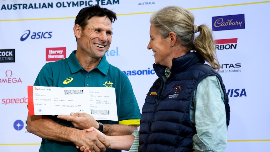 Equestrian Shane Rose holds a large boarding pass and smiles while shaking a woman's hand.