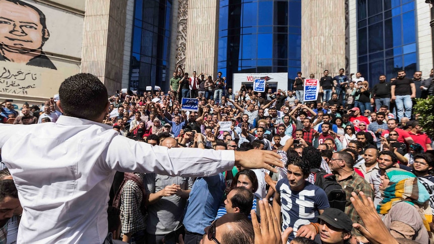 Hundreds of Egyptians crowd together in front of a building, many holding signs.