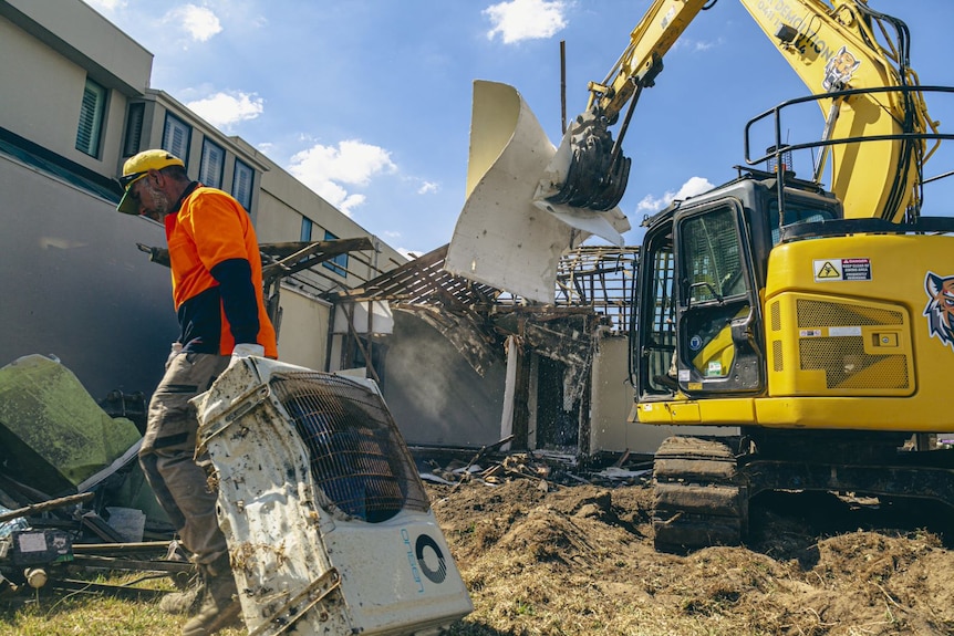 A tradie pulls an old air-conditioning unit away from a building site