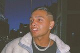 A young Aboriginal man wearing a jacket and a silver chain necklace