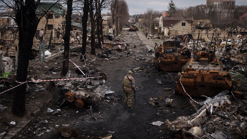 A soldier walks along a road littered with war wreckage, with bits of homes, vechiles and other structures strewn everywhere.