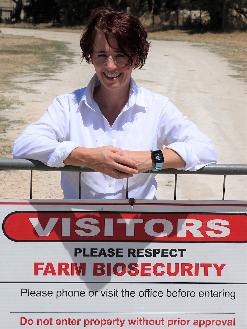 Margo Andrae leans on a farm fence with a biosecurity sign attached.