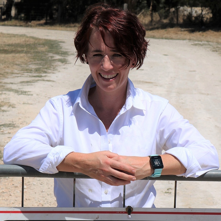 Margo Andrae leans on a farm fence with a biosecurity sign attached.