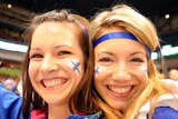two Finnish ice hockey fans with the Finland flag painted on their face smile at the camera