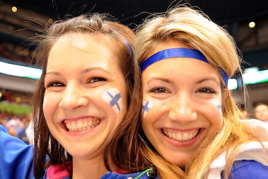 two Finnish ice hockey fans with the Finland flag painted on their face smile at the camera