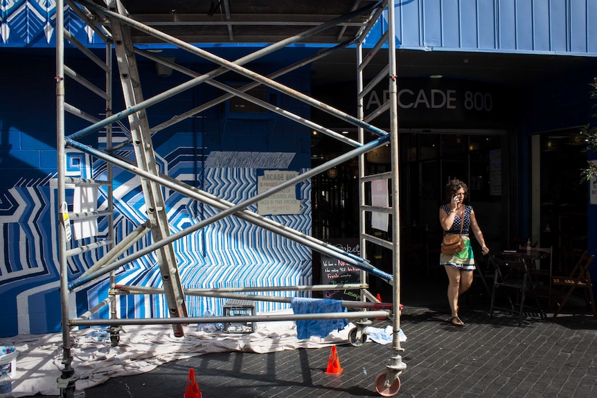 A woman walks past Lucas Grogan's street artwork in progress in Wolf Lane