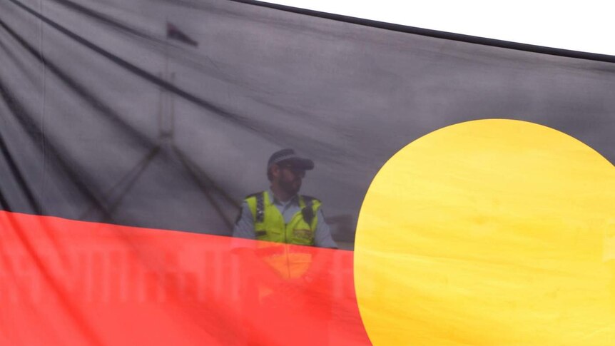 A semi-transparent indigenous flag in front of a police officer, with Parliament House in the background.