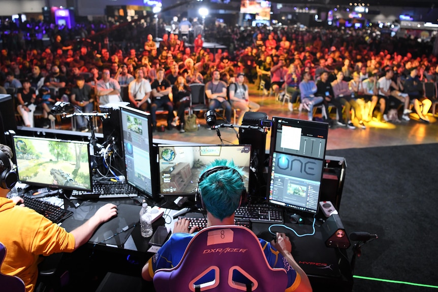 A man with bright blue hair at a computer in front of a crowd