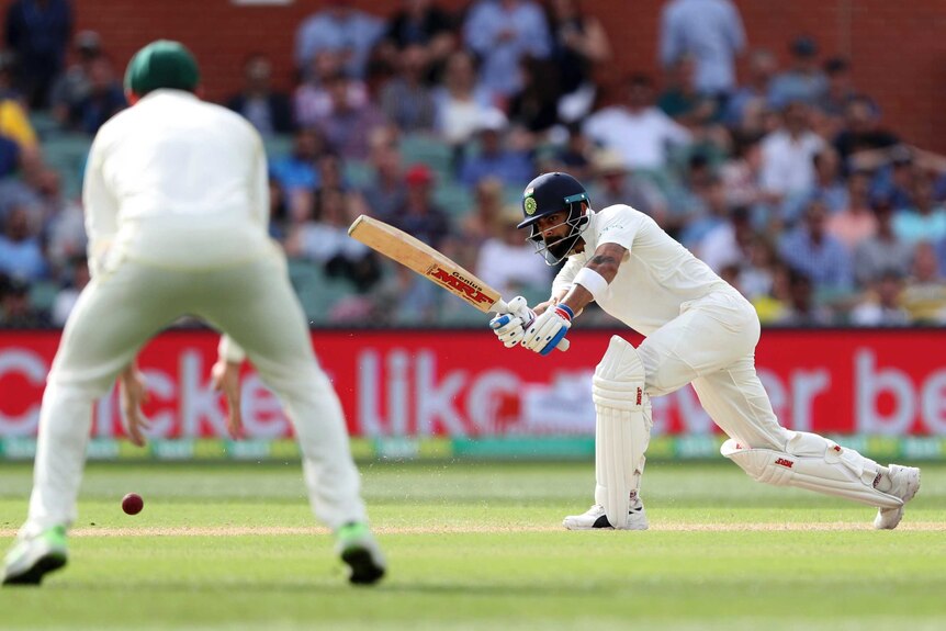 India batsman Virat Kohli plays a cricket shot as an Australian fielder looks on.