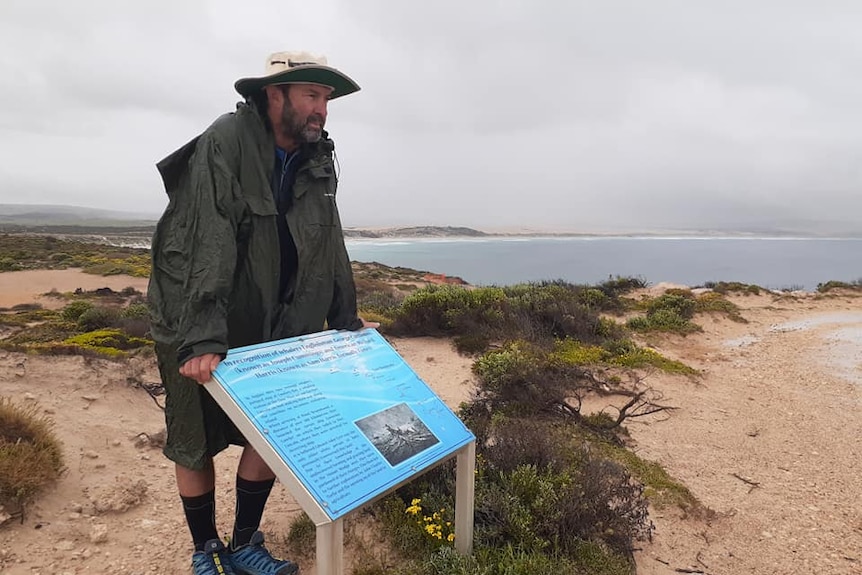 Man leaning on sign on cliff overlooking beach