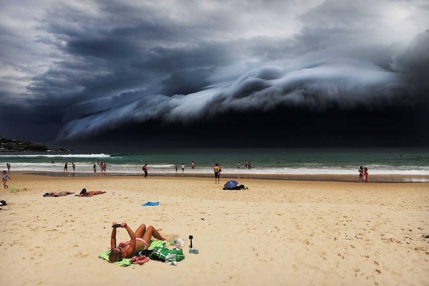 A massive 'cloud tsunami' looms over Sydney as a sunbather reads on Bondi Beach.
