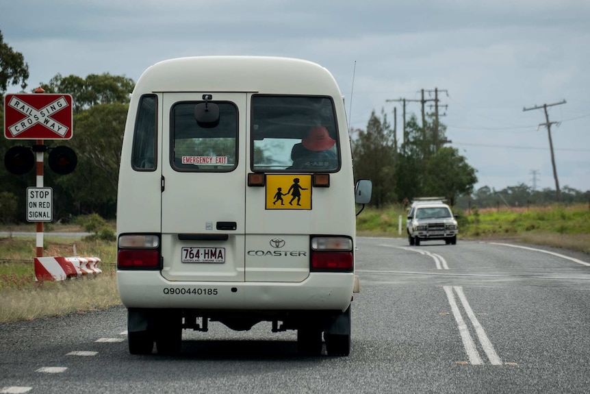 A school bus drives past a train crossing on a country road