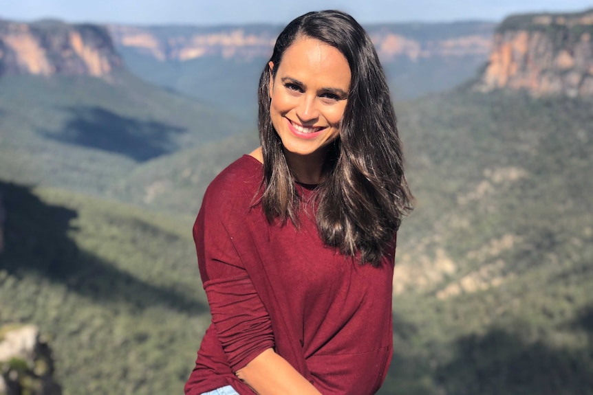 Patricia Goncalves in maroon top, sitting in front of a mountain range valley.