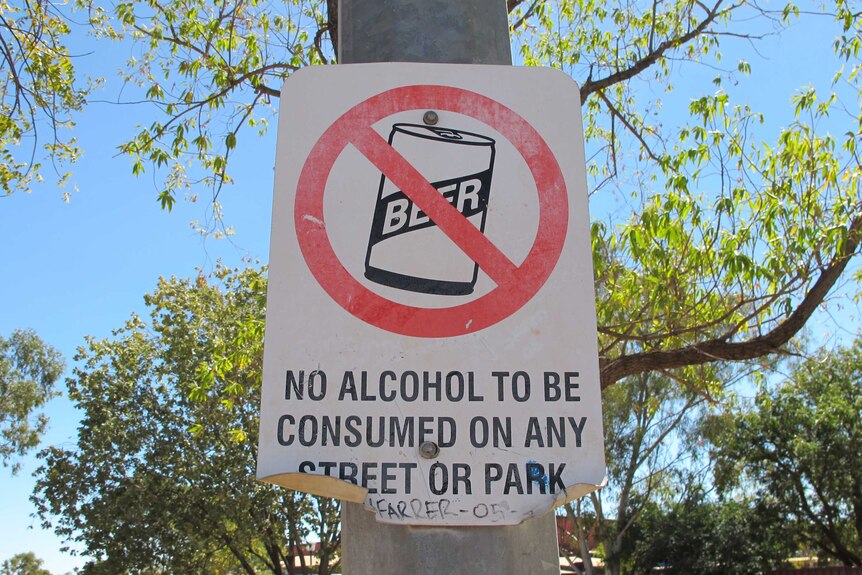 A sign with a no-drinking symbol warning of alcohol restrictions in a town.