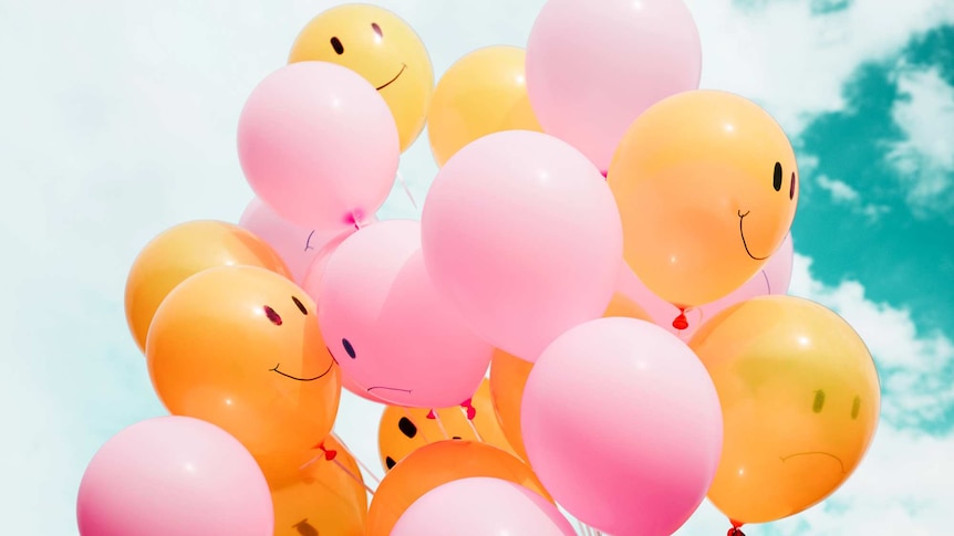 Smiley and sad face balloons against a cloudy blue sky for story on rethinking stress