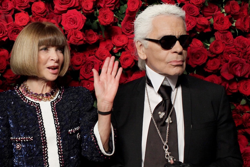 Anna Wintour and Karl Lagerfeld stand together in front of a wall of red roses.