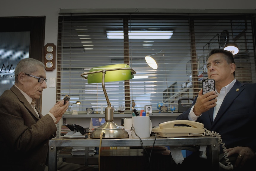 An elderly man looks at a phone sitting at a desk across from private investigator Rómulo Aitken in documentary The Mole Agento