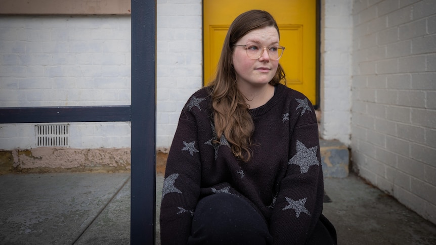 A young woman with glasses sits on a front step