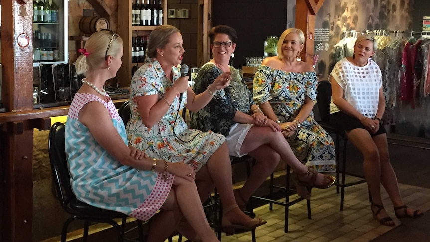 Five women sit on stools, one speaking into a microphone, while addressing Barkly Women's Day