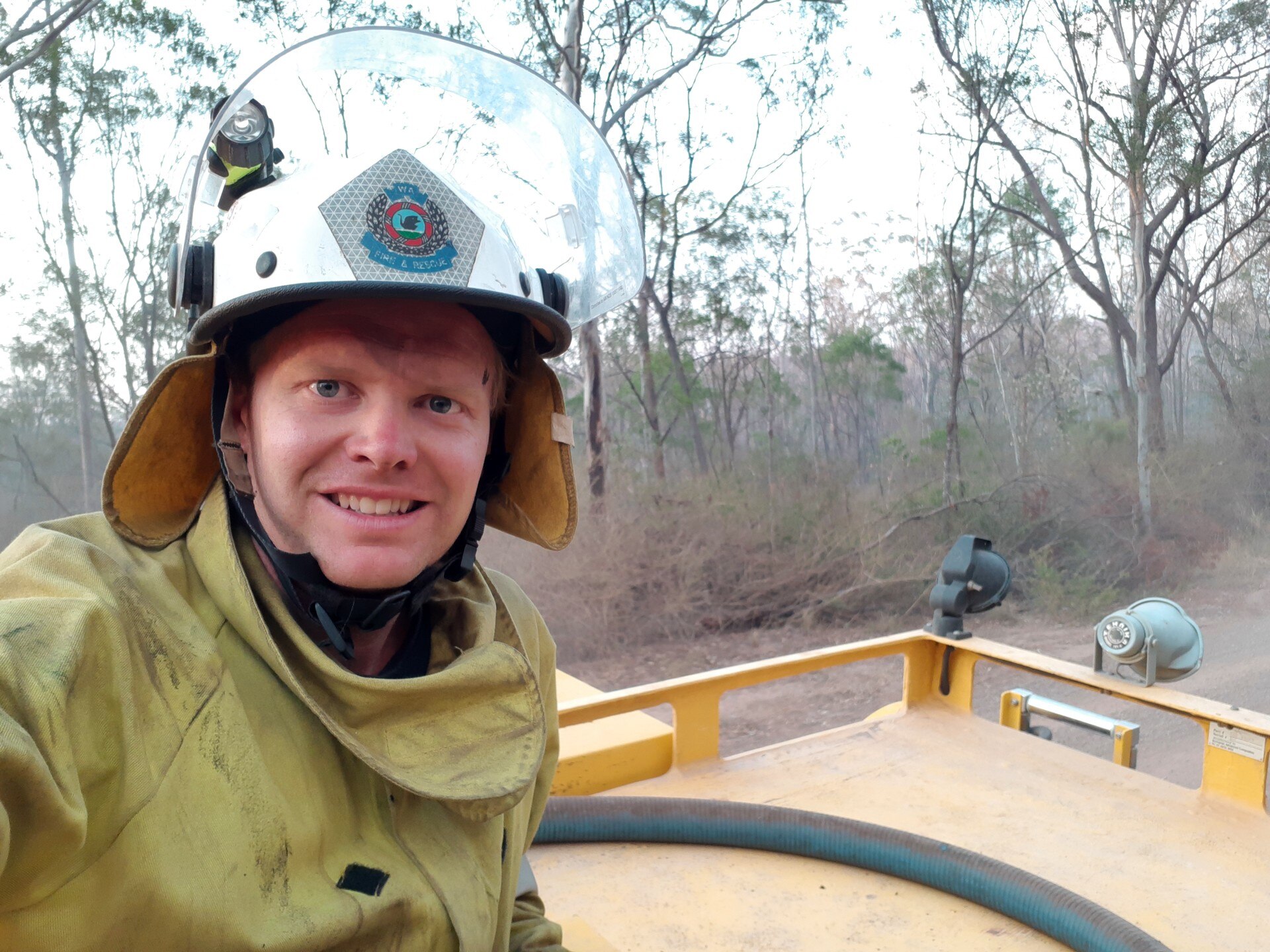 Un hombre con uniforme de bombero en la parte trasera de un camión en el lugar de un incendio. 