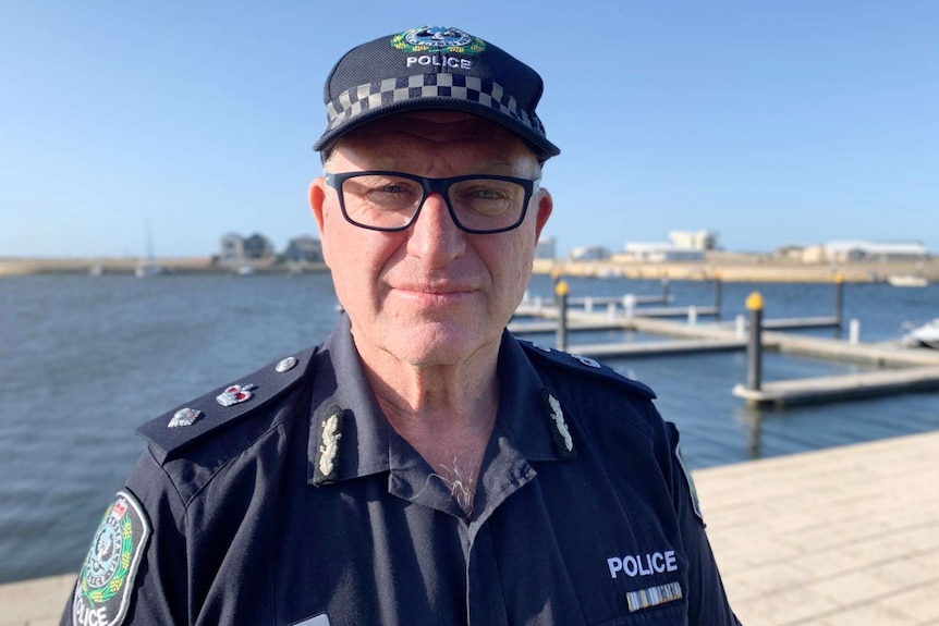 A man in police uniform wearing glasses stands with a marina behind him