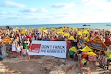 A wide shot of anti-fracking protestors carrying banners and placards at Broome’s Entrance Point beach.
