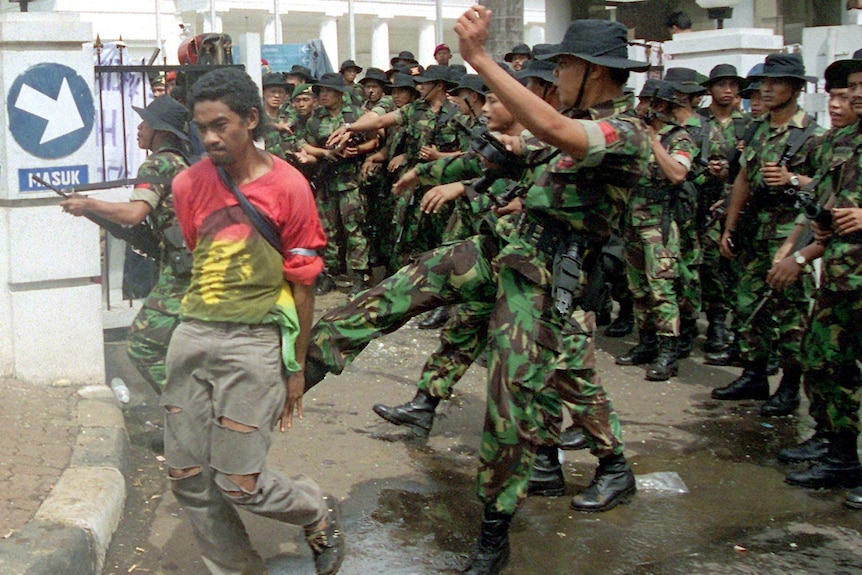 A soldier kicks a student in the backside in front of a line of soldiers to the gates of the foreign ministry